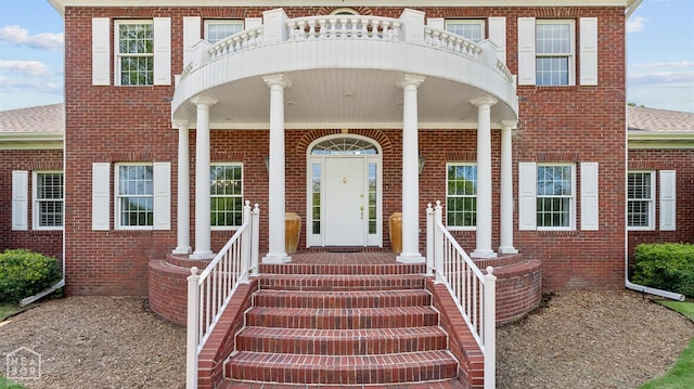 entrance to property featuring brick siding, a shingled roof, and covered porch