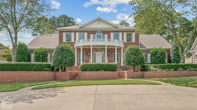 colonial-style house with a balcony, brick siding, and a front lawn