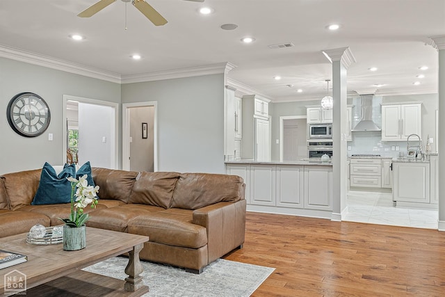 living room featuring crown molding, a ceiling fan, recessed lighting, light wood-style floors, and decorative columns