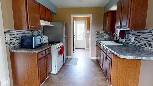 207 11th St, Marked Tree, AR 72365 - kitchen with under cabinet range hood, white range with gas cooktop, black microwave, backsplash, and brown cabinets