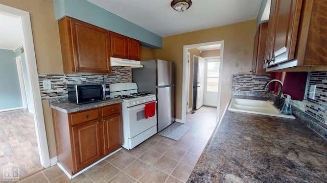 207 11th St, Marked Tree, AR 72365 - kitchen with white gas stove, under cabinet range hood, backsplash, freestanding refrigerator, and brown cabinetry