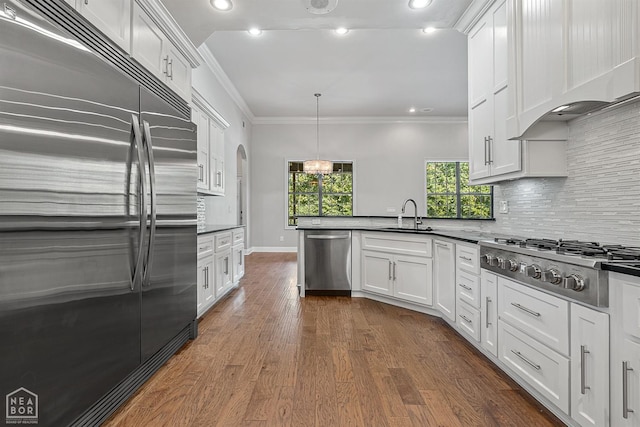 kitchen with a peninsula, appliances with stainless steel finishes, crown molding, and dark countertops