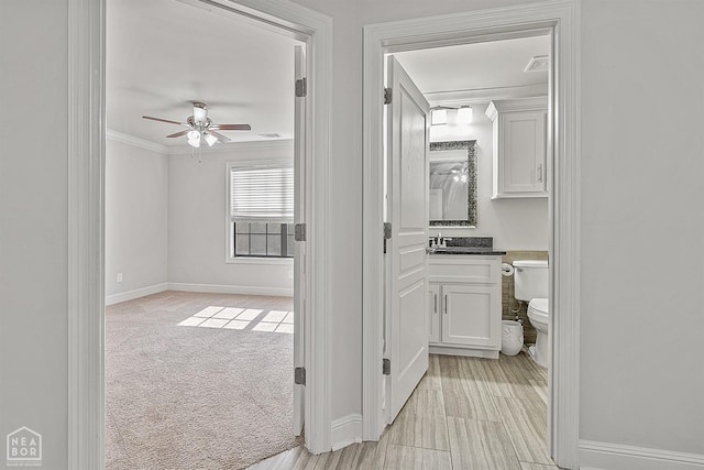 hall with light colored carpet, baseboards, and ornamental molding