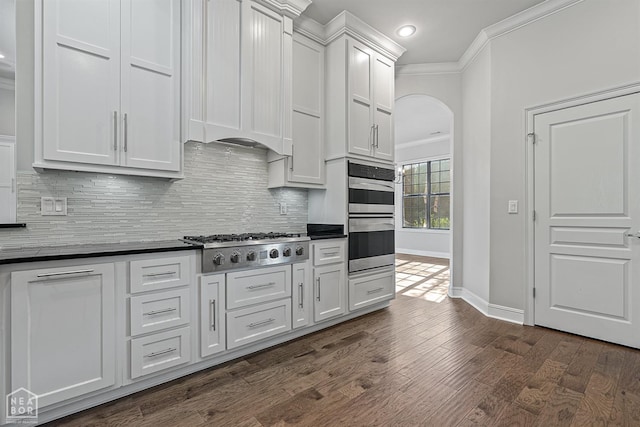 kitchen with arched walkways, ornamental molding, dark countertops, stainless steel appliances, and decorative backsplash