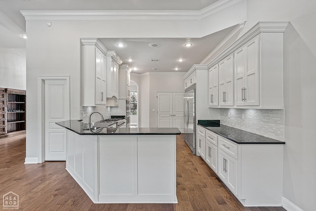 kitchen featuring white cabinets, arched walkways, stainless steel built in fridge, and dark countertops