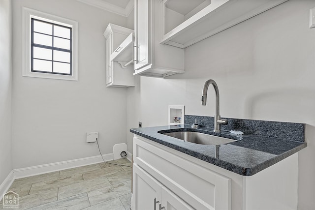 kitchen featuring baseboards, crown molding, white cabinets, dark stone counters, and a sink