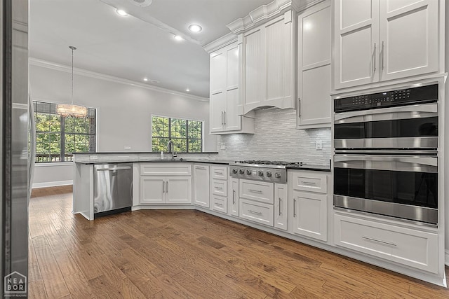 kitchen featuring dark wood-style flooring, a peninsula, crown molding, stainless steel appliances, and backsplash