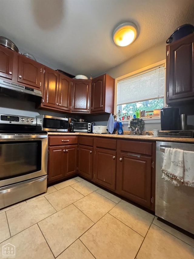 kitchen featuring under cabinet range hood, stainless steel appliances, light tile patterned floors, and light countertops