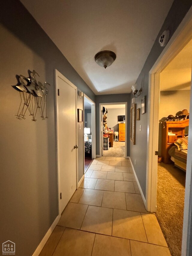 corridor with tile patterned floors, baseboards, and carpet