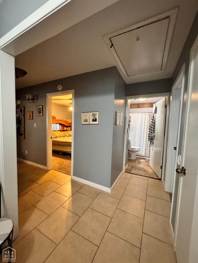 hall with baseboards, attic access, and light tile patterned floors