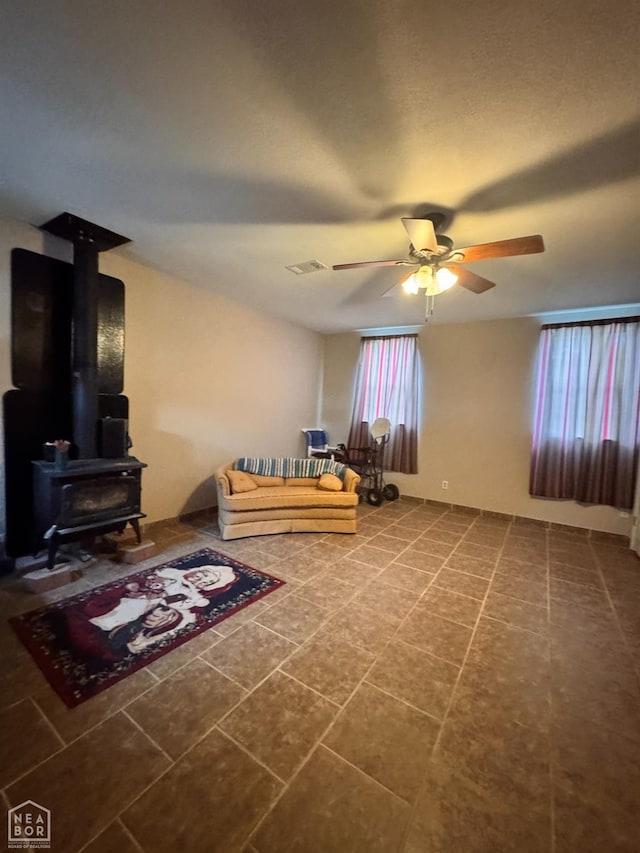 living room with a ceiling fan, a wood stove, and visible vents