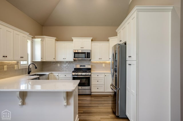 kitchen with white cabinets, appliances with stainless steel finishes, a sink, a peninsula, and lofted ceiling