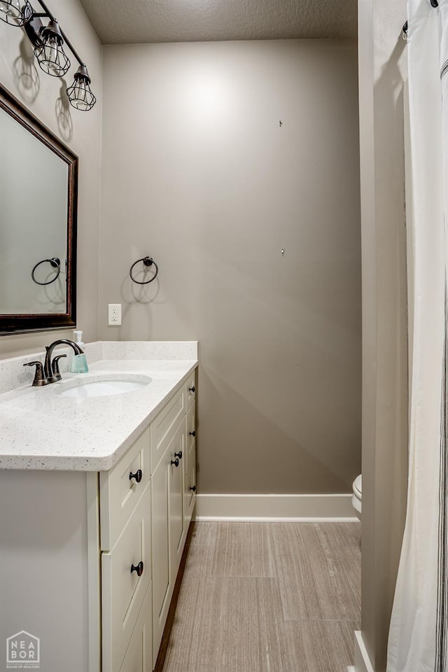 bathroom featuring toilet, baseboards, and vanity
