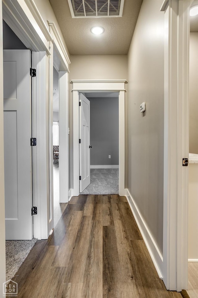 hallway with baseboards, visible vents, and wood finished floors