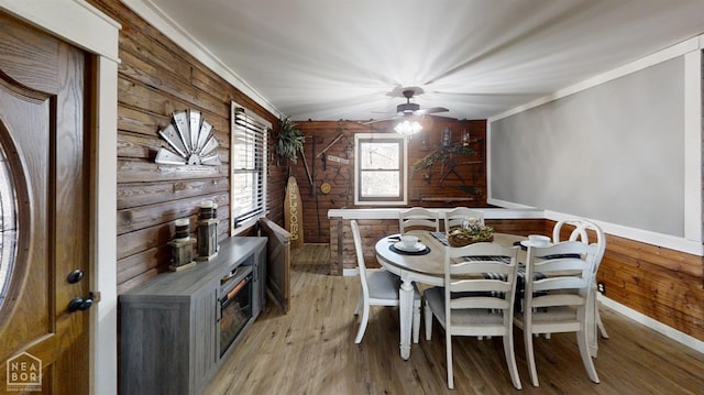 dining space with light wood finished floors, baseboards, ornamental molding, and wooden walls