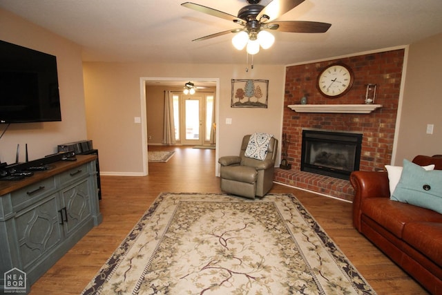living room featuring ceiling fan, baseboards, wood finished floors, and a fireplace