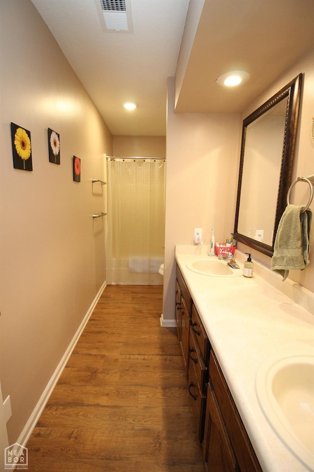 bathroom with visible vents, baseboards, a sink, double vanity, and wood finished floors
