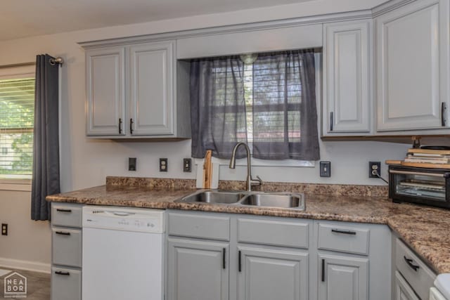 kitchen featuring white dishwasher, dark countertops, baseboards, and a sink