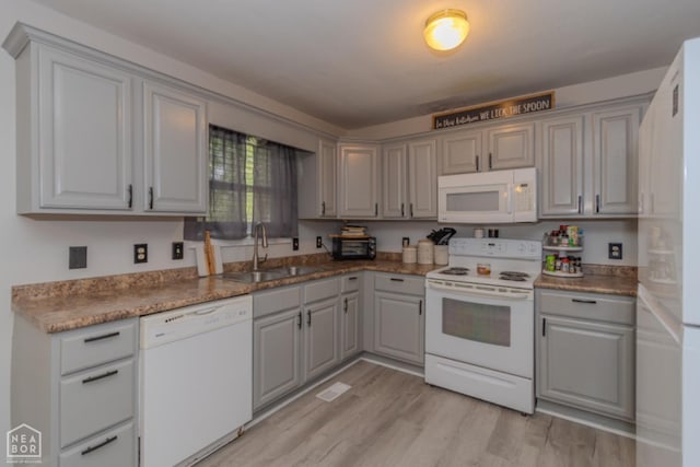 kitchen with a sink, gray cabinets, white appliances, and light wood-style flooring