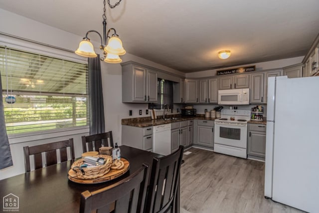 kitchen with an inviting chandelier, dark countertops, white appliances, a sink, and gray cabinetry