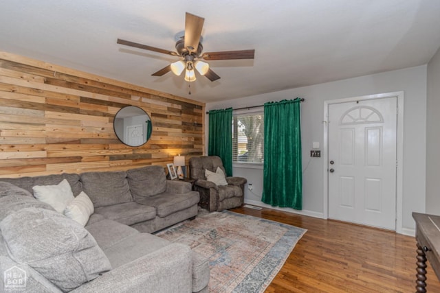 living room featuring a ceiling fan, baseboards, wood walls, and wood finished floors