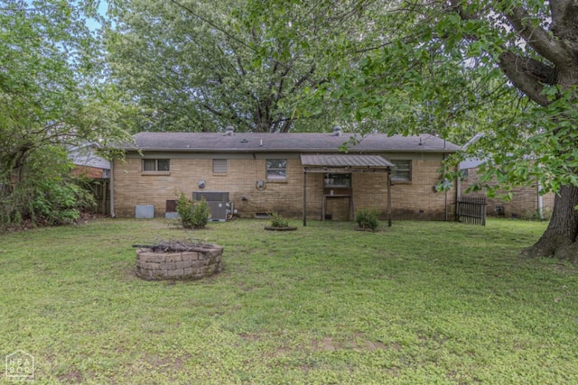 back of property with central AC, a fire pit, fence, and a yard