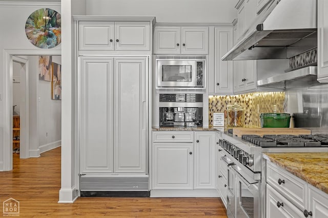 3500 Big Creek Cv, Jonesboro, AR 72404 - kitchen with under cabinet range hood, built in appliances, light wood-type flooring, light stone counters, and white cabinetry
