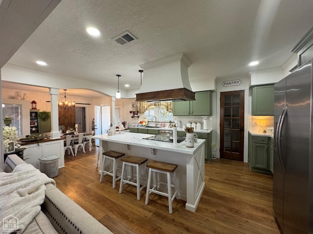 kitchen with freestanding refrigerator, green cabinets, ornate columns, visible vents, and a sink