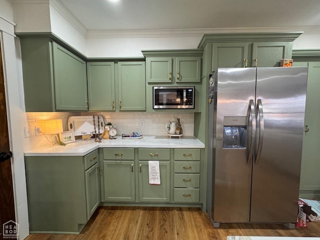kitchen with green cabinetry, stainless steel appliances, light wood-style flooring, and decorative backsplash
