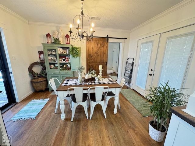 dining area with visible vents, a barn door, ornamental molding, a chandelier, and wood finished floors