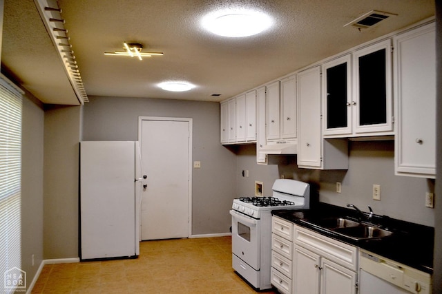 kitchen with white appliances, white cabinets, visible vents, a sink, and dark countertops