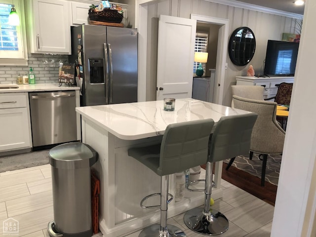 kitchen with appliances with stainless steel finishes, decorative backsplash, a breakfast bar, and white cabinetry