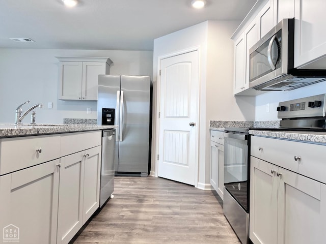 112 Terry Dr, Brookland, AR 72417 - kitchen with stainless steel appliances, light wood-style flooring, a sink, light stone countertops, and white cabinetry