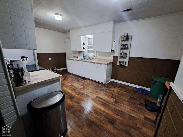 kitchen featuring dark wood finished floors, white cabinets, visible vents, wainscoting, and brick wall