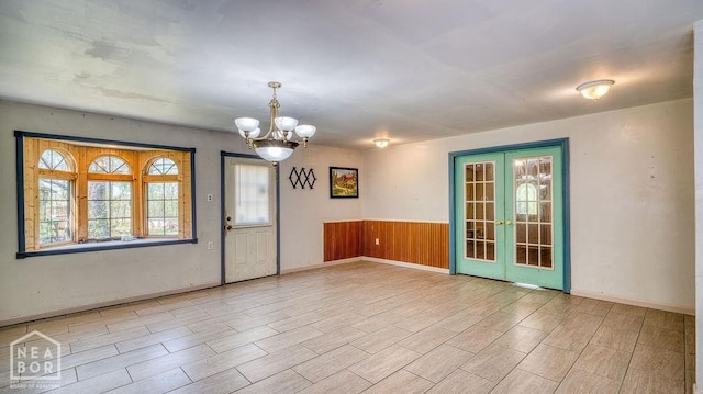 unfurnished room featuring french doors, wood tiled floor, a notable chandelier, and a wainscoted wall