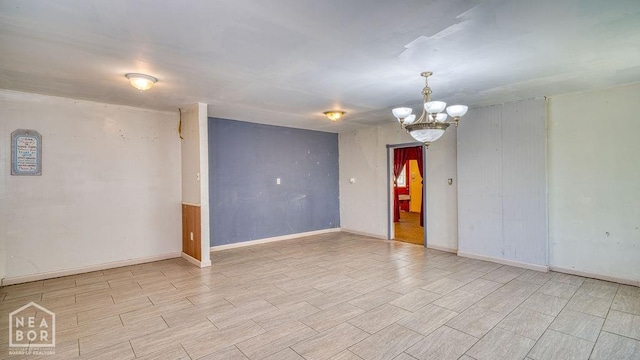 empty room featuring wood finish floors, baseboards, and a notable chandelier