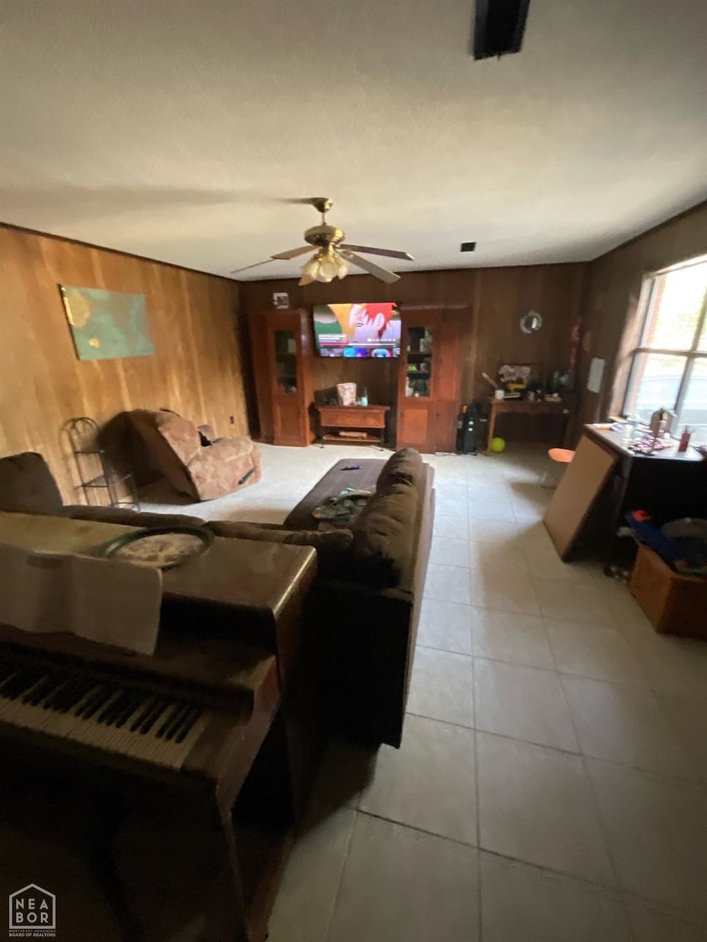 living room featuring wood walls, a ceiling fan, and light tile patterned floors