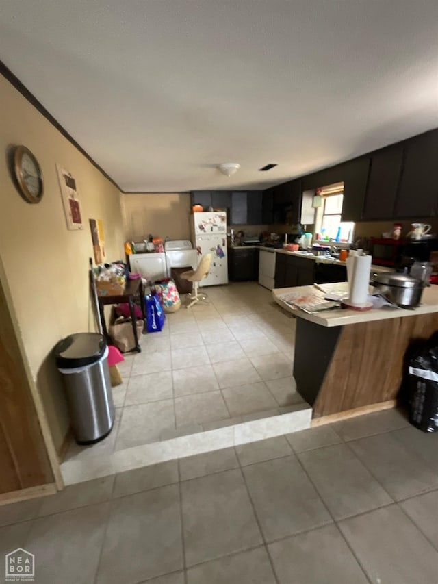 kitchen featuring dark cabinets, a peninsula, freestanding refrigerator, and light tile patterned floors