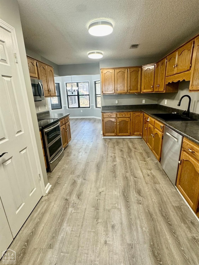 3426 Aggie Rd, Jonesboro, AR 72405 - kitchen with a sink, appliances with stainless steel finishes, light wood-style floors, brown cabinets, and a textured ceiling
