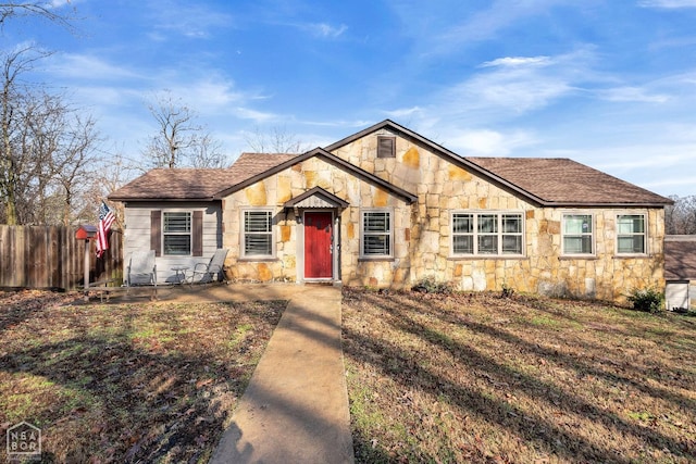 view of front facade featuring roof with shingles, stone siding, and fence