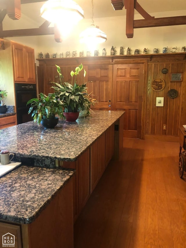  - kitchen with dark stone counters, dobule oven black, brown cabinetry, a kitchen island, and wood finished floors