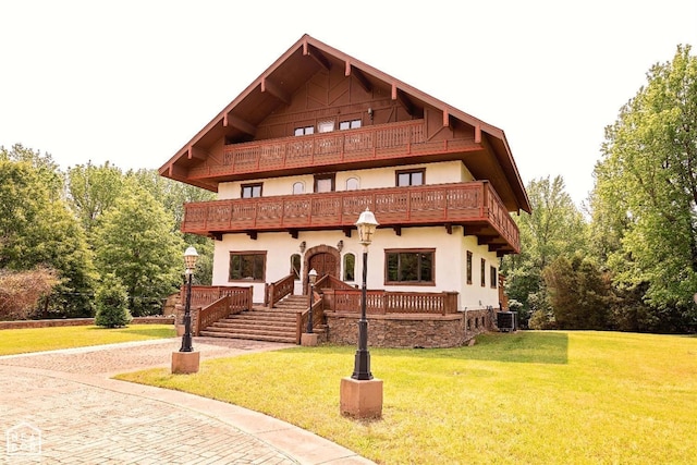  - view of front of home featuring a balcony, stucco siding, a front yard, stairs, and central AC