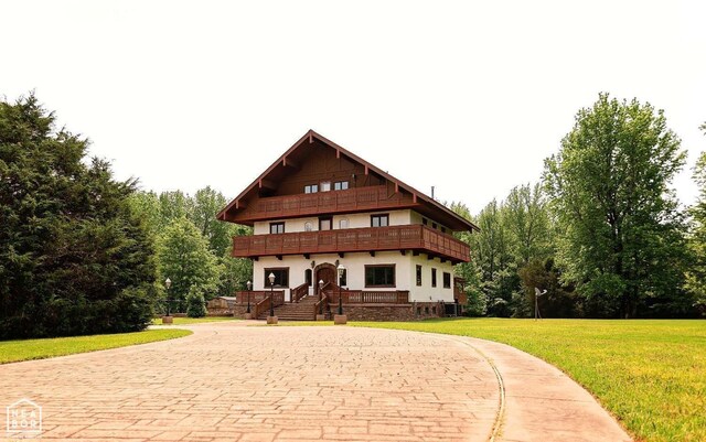 - view of front of property with a balcony, central air condition unit, curved driveway, stucco siding, and a front lawn