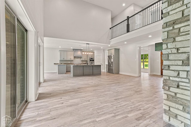 unfurnished living room featuring recessed lighting, light wood finished floors, a high ceiling, and baseboards