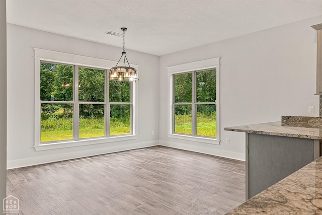 unfurnished dining area featuring an inviting chandelier, a textured ceiling, visible vents, wood finished floors, and baseboards