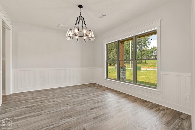 unfurnished dining area with visible vents, a wainscoted wall, a notable chandelier, and wood finished floors