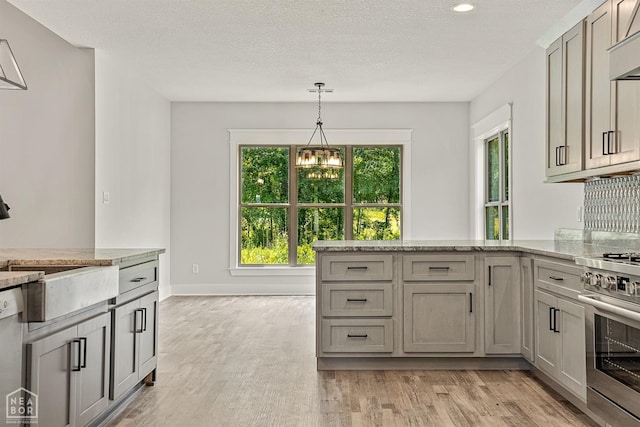 kitchen with light wood finished floors, decorative light fixtures, a chandelier, and stainless steel stove