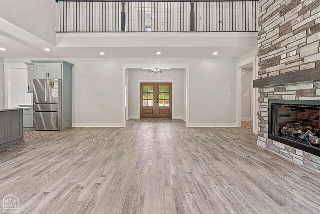 unfurnished living room with french doors, light wood finished floors, a high ceiling, and baseboards