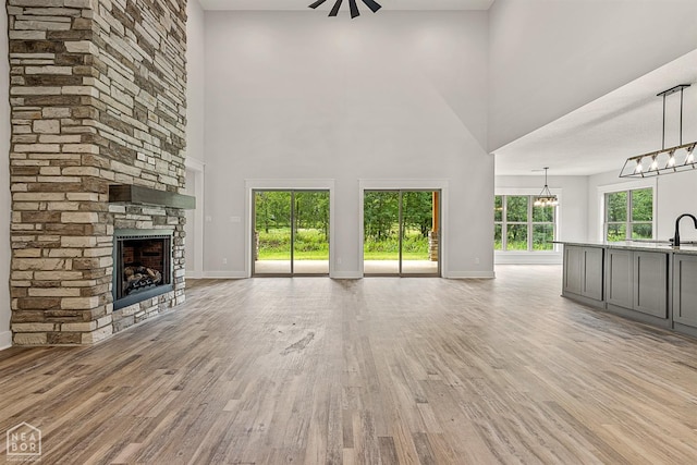 unfurnished living room featuring baseboards, light wood finished floors, a notable chandelier, and a stone fireplace