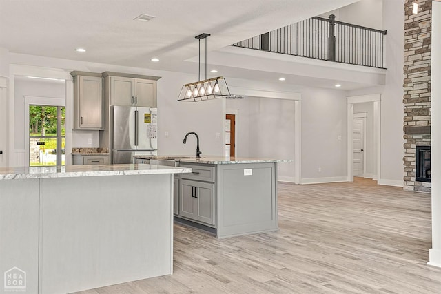 kitchen with light wood finished floors, gray cabinets, freestanding refrigerator, and an island with sink